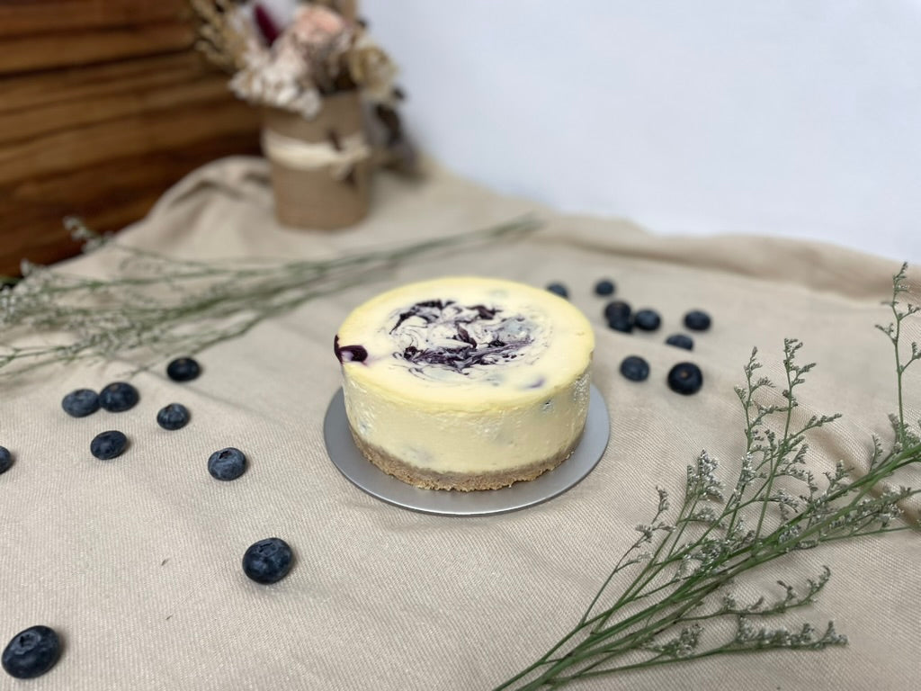 Cheesecake with blueberries on a textured surface with flowers in the background